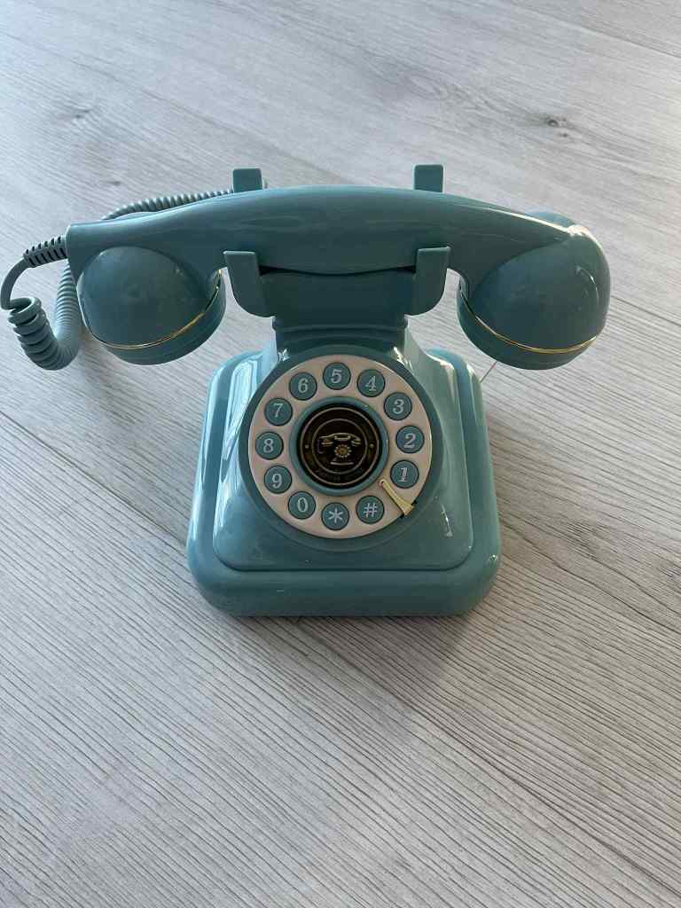A vintage blue rotary dial phone positioned on a wooden surface.