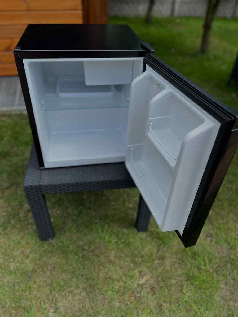 Compact black refrigerator with an open door, showing its empty interior and a small shelf.
