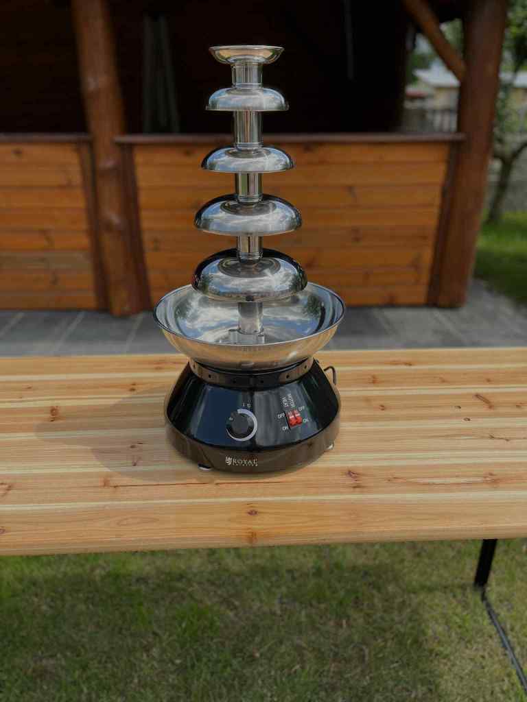 Chocolate fountain on a wooden table in an outdoor setting.