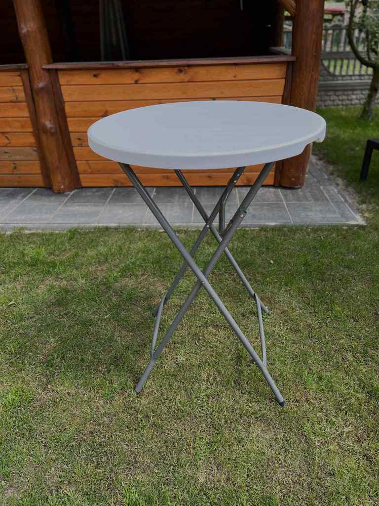 A gray round folding table positioned on grass with a wooden structure in the background.