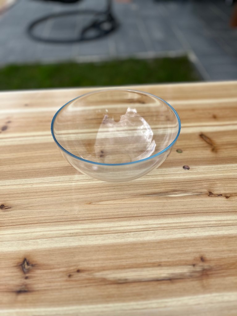 Clear glass bowl on a wooden table with green grass visible in the background.