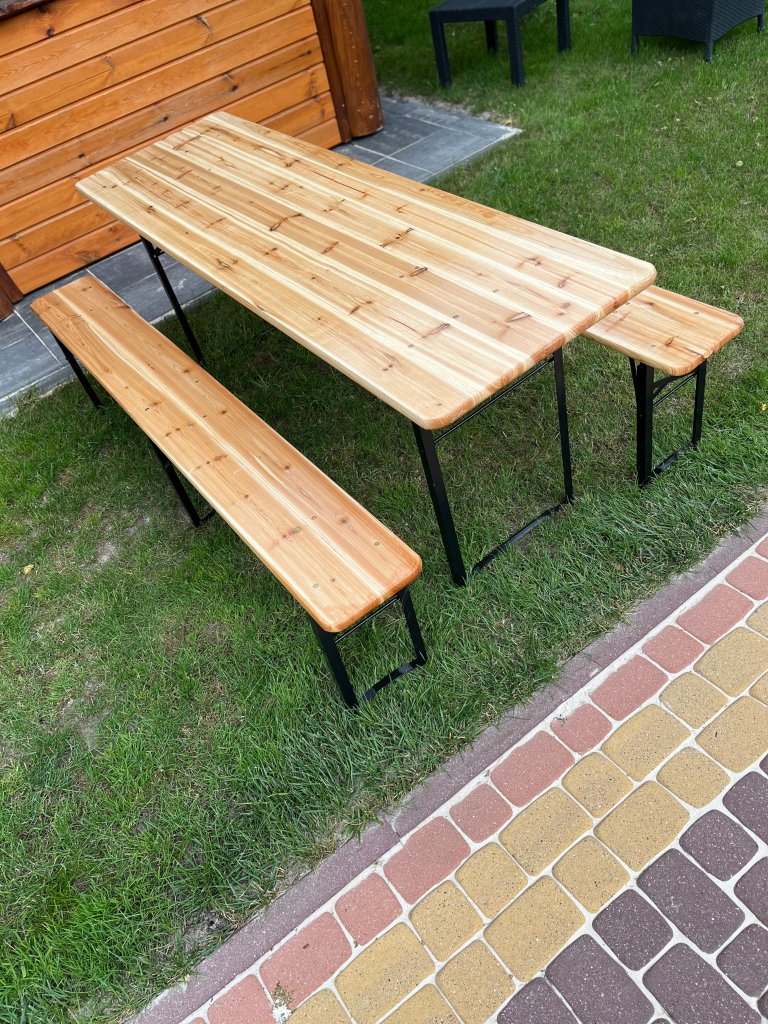 A wooden outdoor dining table with two matching benches, set on a grassy area with a stone pathway nearby.